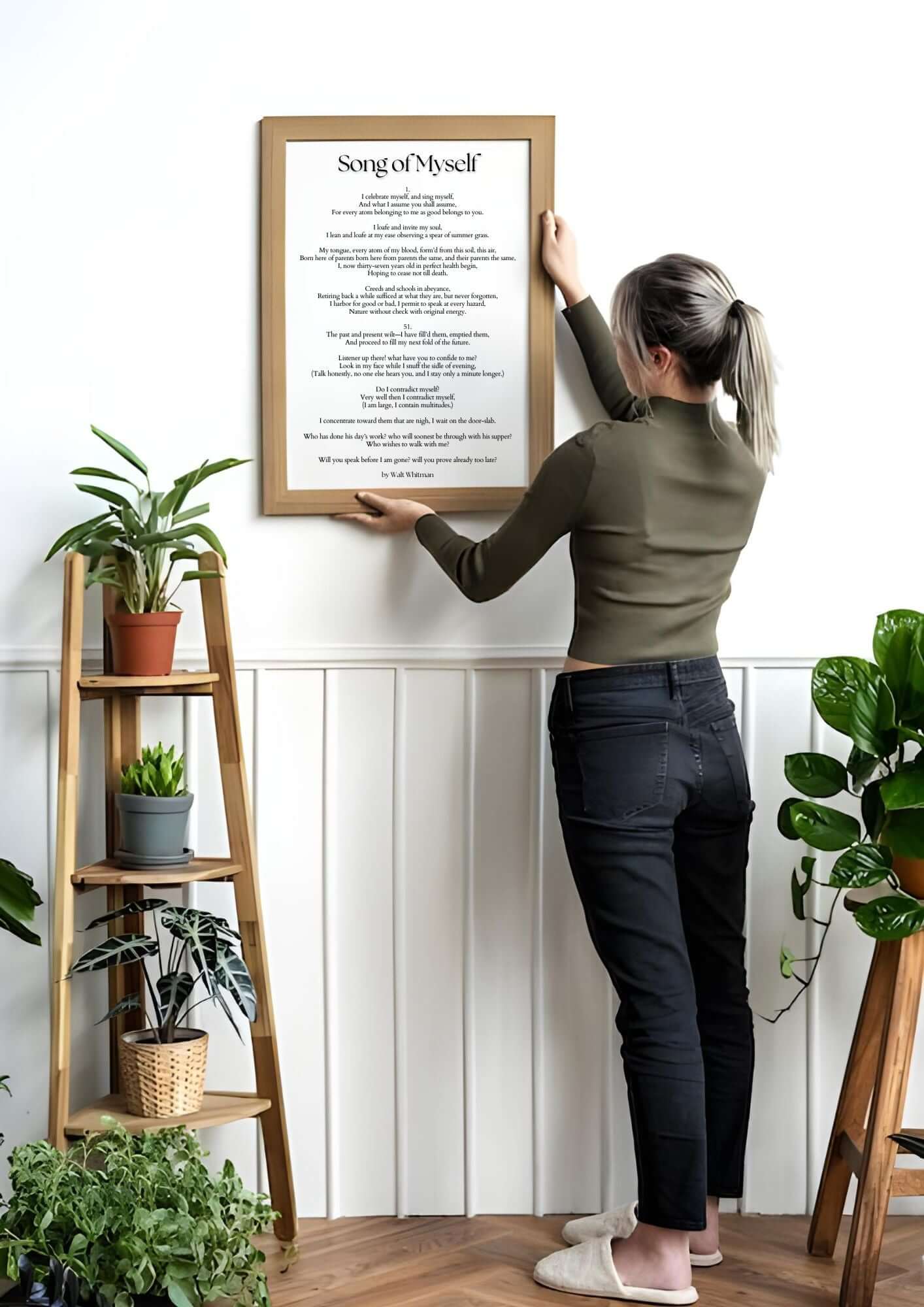 Woman hanging 'Song of Myself' by Walt Whitman – Inspirational Poetry Printable Wall Art on white wall with plants