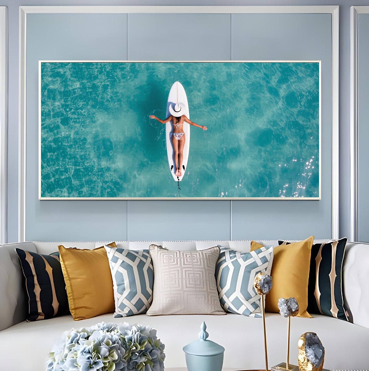 Surfboard Woman Aerial Ocean Print – Minimalist Beach Wall Art featuring a serene woman floating on turquoise waters displayed above a sofa.