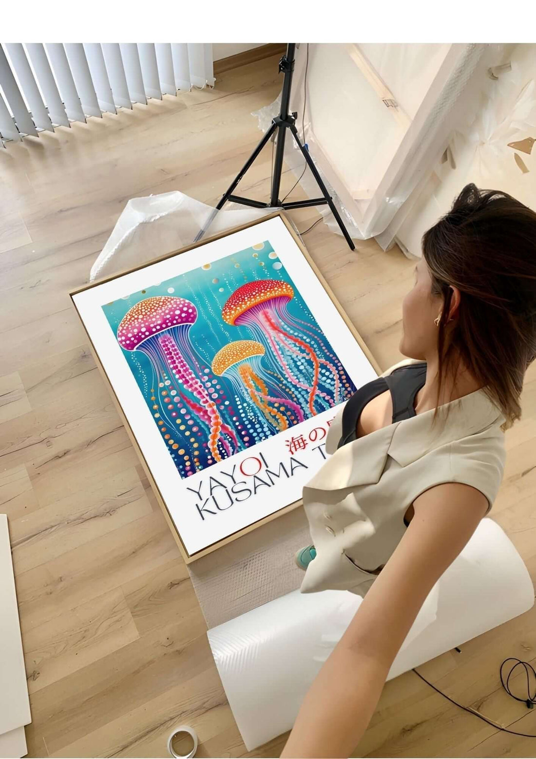 Woman admiring colorful Yayoi Kusama-inspired wall art featuring vibrant jellyfish on a wooden floor in an art studio.
