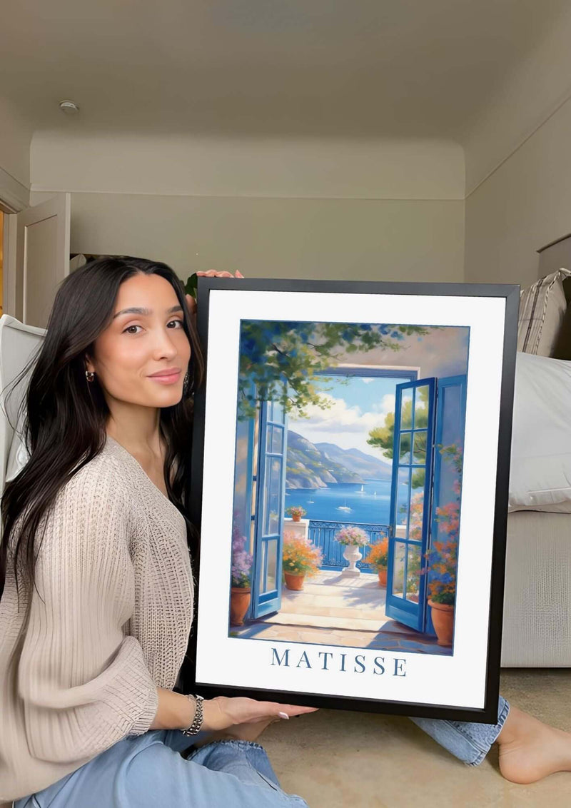 Woman holding framed Henri Matisse digital art print, showcasing vibrant coastal landscape.