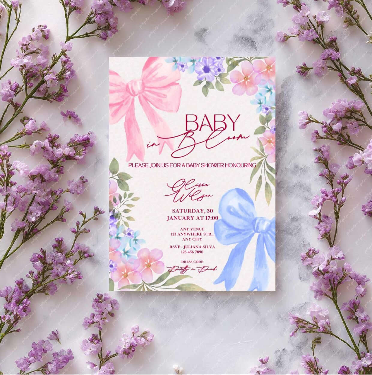 Baby in Bloom Baby Shower Invitation with pink floral designs, watercolor flowers, and elegant bows, displayed on a marble surface.