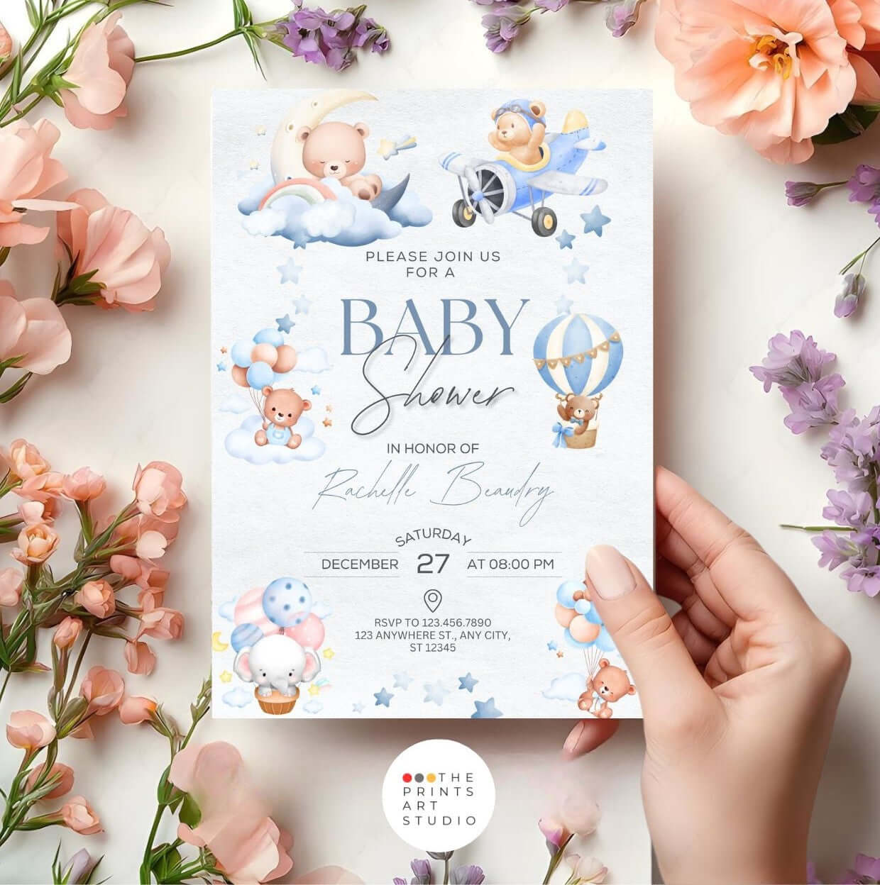 Baby shower invitation with blue and pink designs, surrounded by pastel flowers and held by a hand.