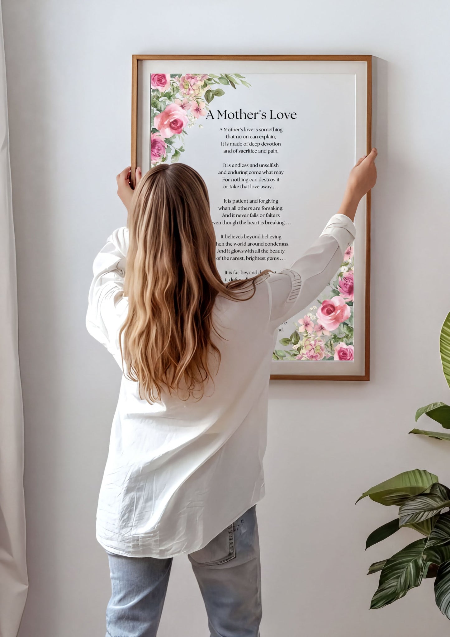 A woman adjusting the Mothers Love Poem Print framed wall art with floral design.