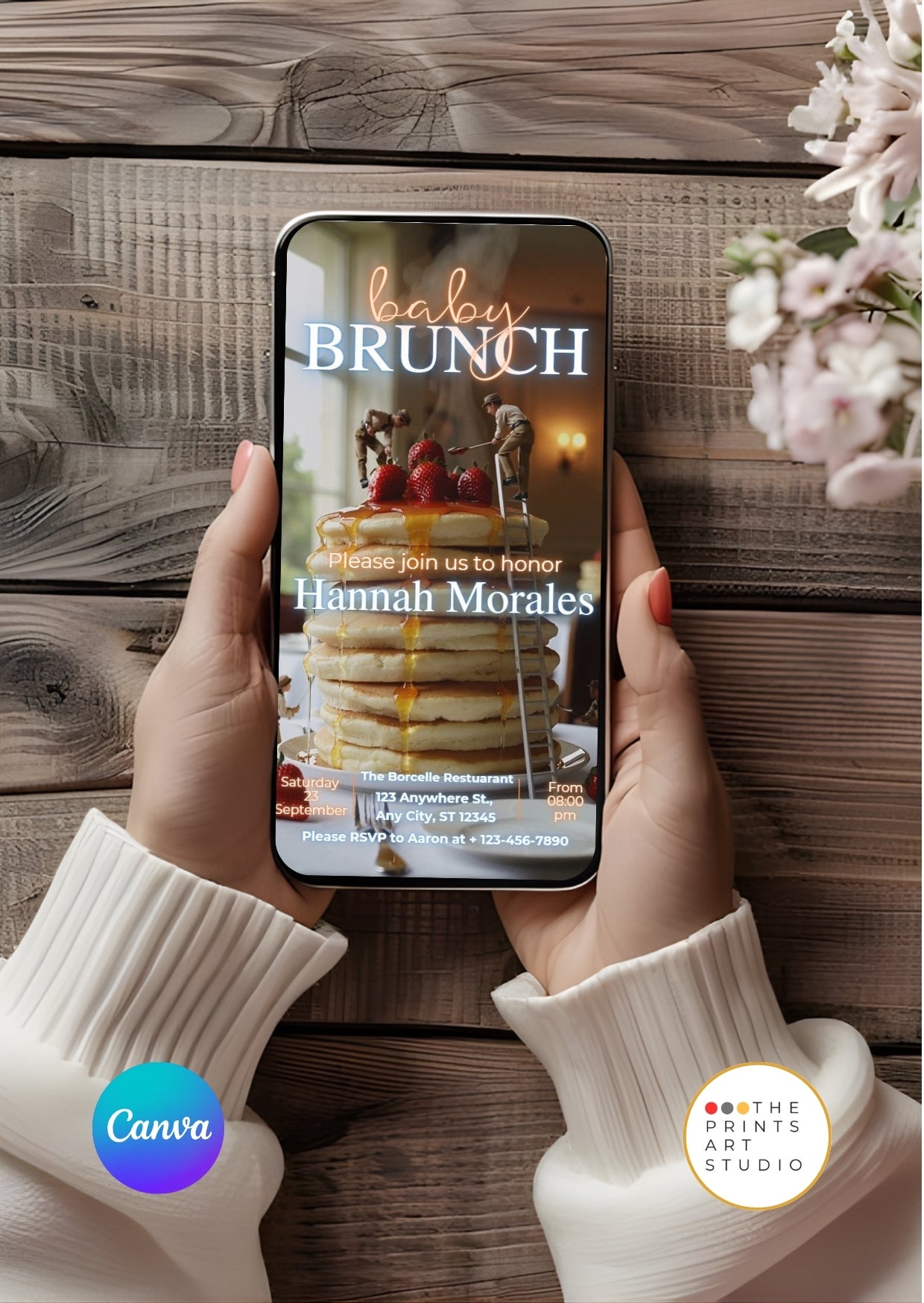 Hands holding a phone displaying a Baby Shower Video Invitation Dreamy Canva Editable with a brunch theme on a wooden background.